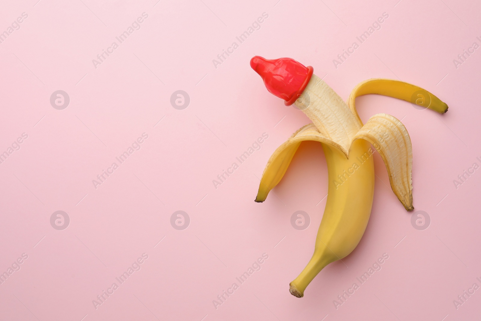 Photo of Banana with condom on pink background, top view and space for text. Safe sex concept