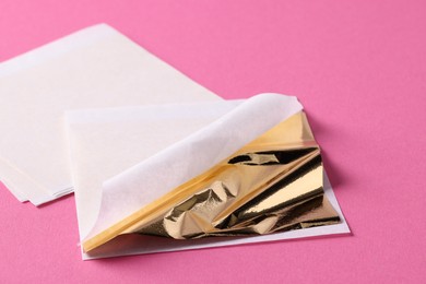 Photo of Edible gold leaf sheets on pink background, closeup