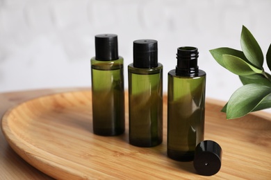 Mini bottles with cosmetic products on wooden tray against white background