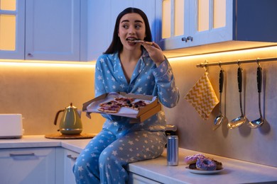 Photo of Young woman eating pizza in kitchen at night. Bad habit