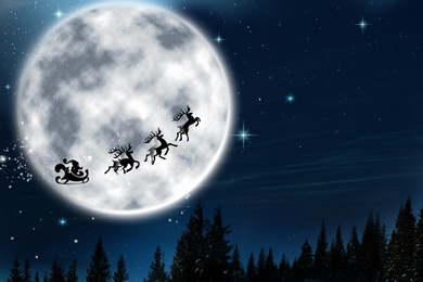 Image of Magic Christmas eve. Santa with reindeers flying in sky on full moon night