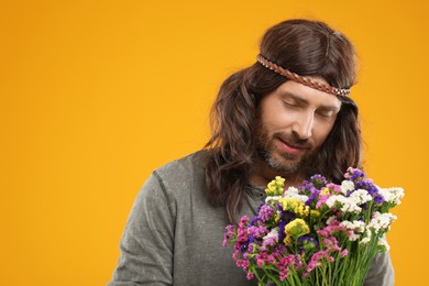 Photo of Hippie man with bouquet of colorful flowers on orange background, space for text
