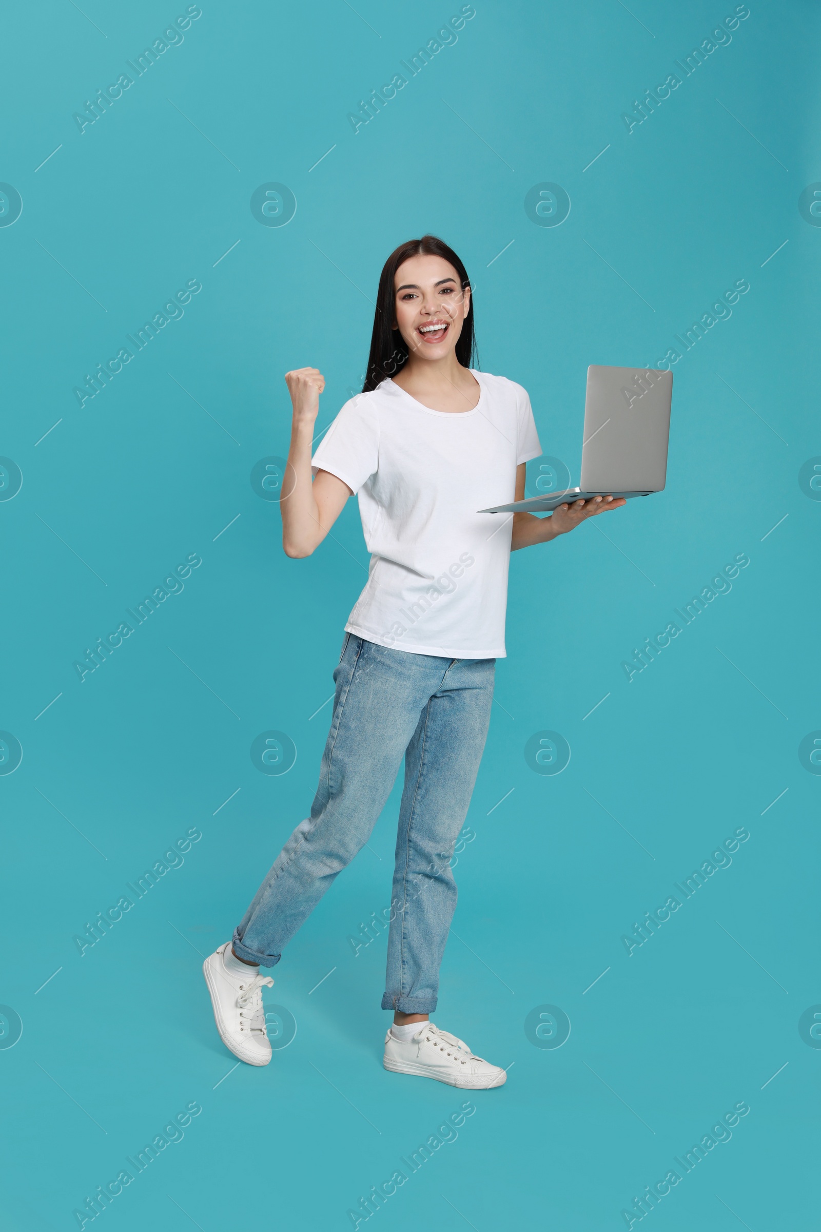 Photo of Emotional young woman with modern laptop on light blue background