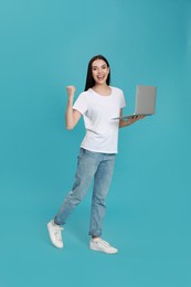 Emotional young woman with modern laptop on light blue background