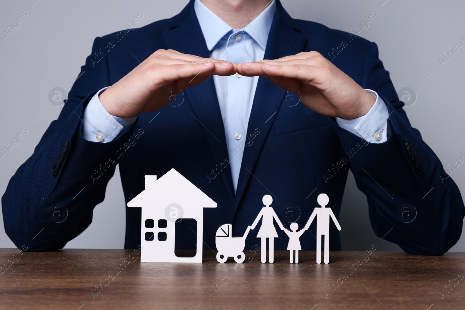 Photo of Man protecting figures of family and house at wooden table. closeup. Insurance concept