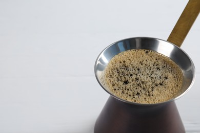 Turkish coffee pot with hot drink on white wooden table, closeup. Space for text