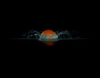 Photo of Tangerine falling down into clear water against black background