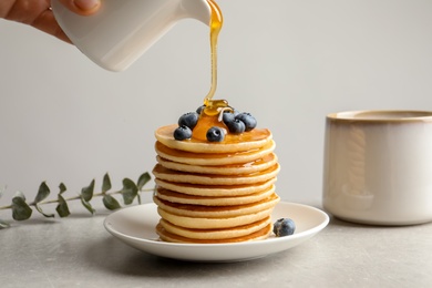 Photo of Woman pouring honey onto tasty pancakes with berries on table, closeup