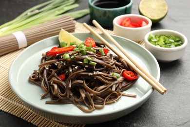 Photo of Tasty buckwheat noodles (soba) with chili pepper, onion and chopsticks on grey table, closeup