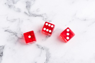 Three red game dices on white marble table, flat lay