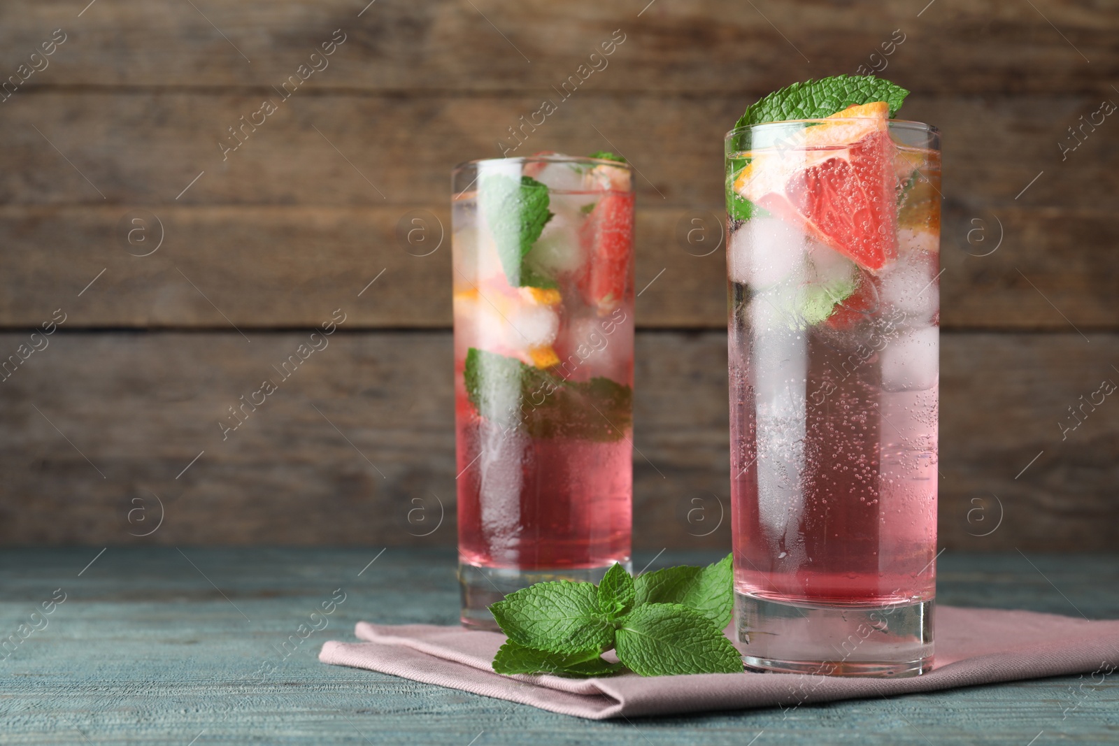 Photo of Delicious grapefruit lemonade with soda water and mint on blue wooden table, space for text. Fresh summer cocktail