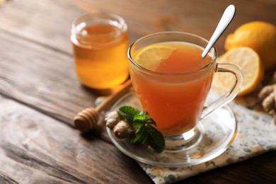 Photo of Cup of delicious ginger tea and ingredients on wooden table, closeup. Space for text