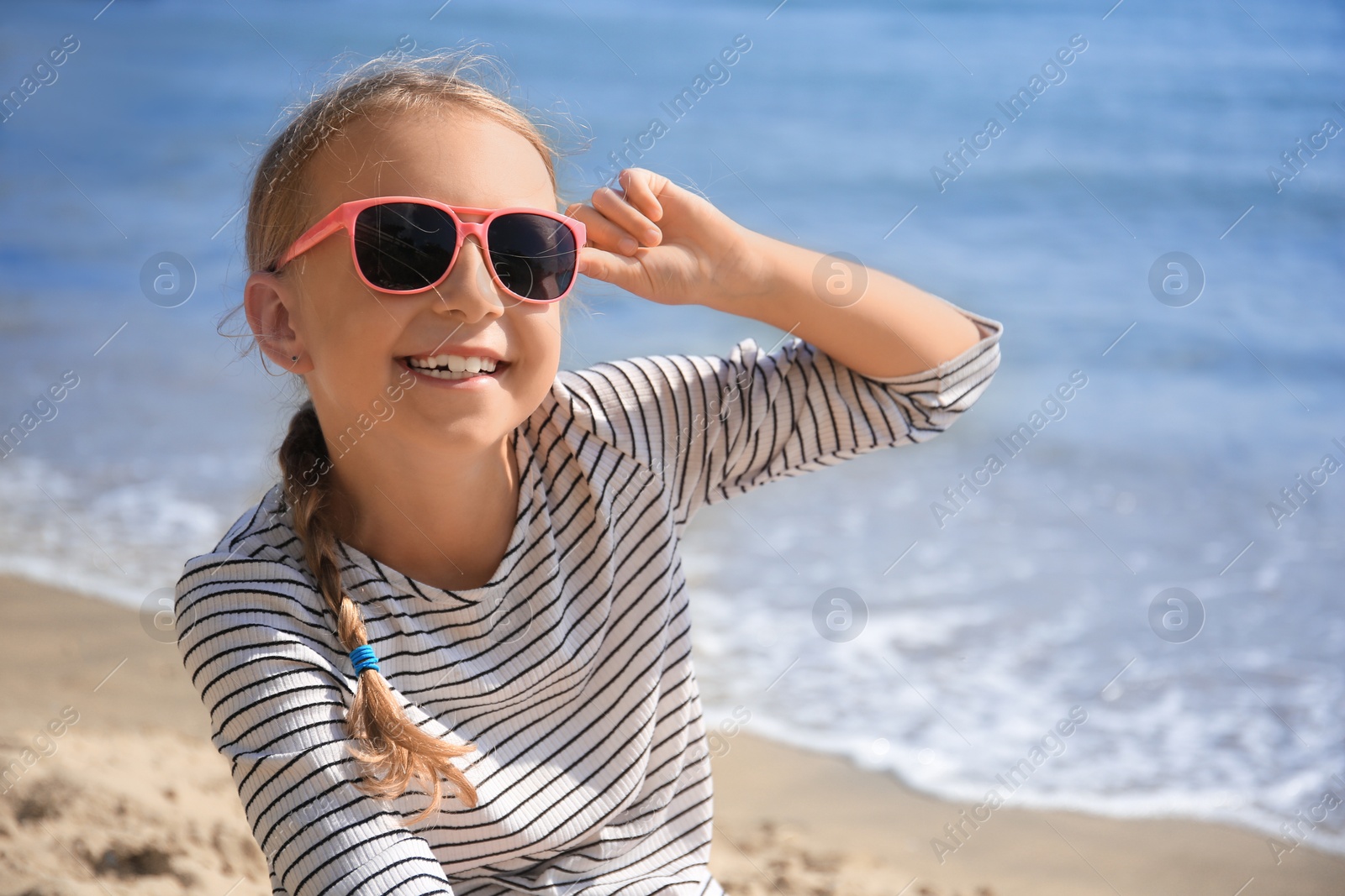 Photo of Happy little girl in stylish sunglasses on beach near sea