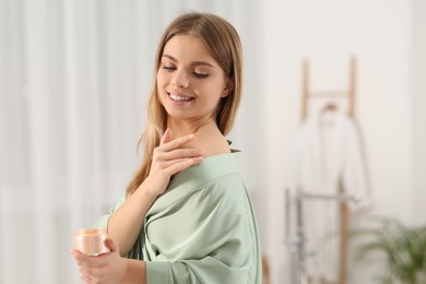 Photo of Beautiful happy woman in stylish robe applying cream in bathroom
