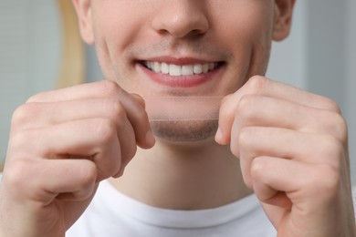 Young man with whitening strip indoors, closeup