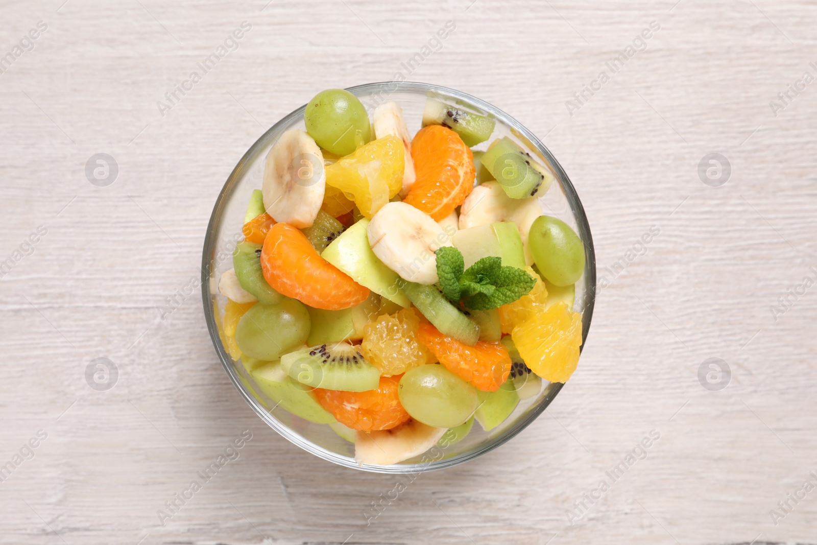 Photo of Delicious fresh fruit salad in bowl on white wooden table, top view