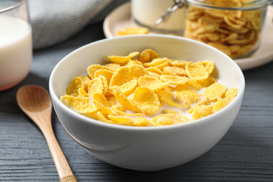 Photo of Tasty crispy corn flakes with milk on grey wooden table, closeup