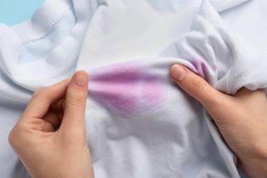 Woman holding white shirt with purple stains on light blue background, closeup