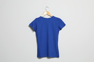 Photo of Hanger with blue t-shirt on light wall. Mockup for design