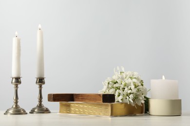 Photo of Burning church candles, wooden cross, Bible and flowers on white table