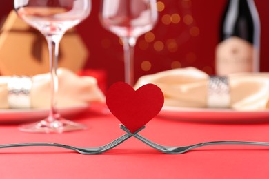 Photo of Joined forks with paper heart on red table, closeup. Romantic dinner