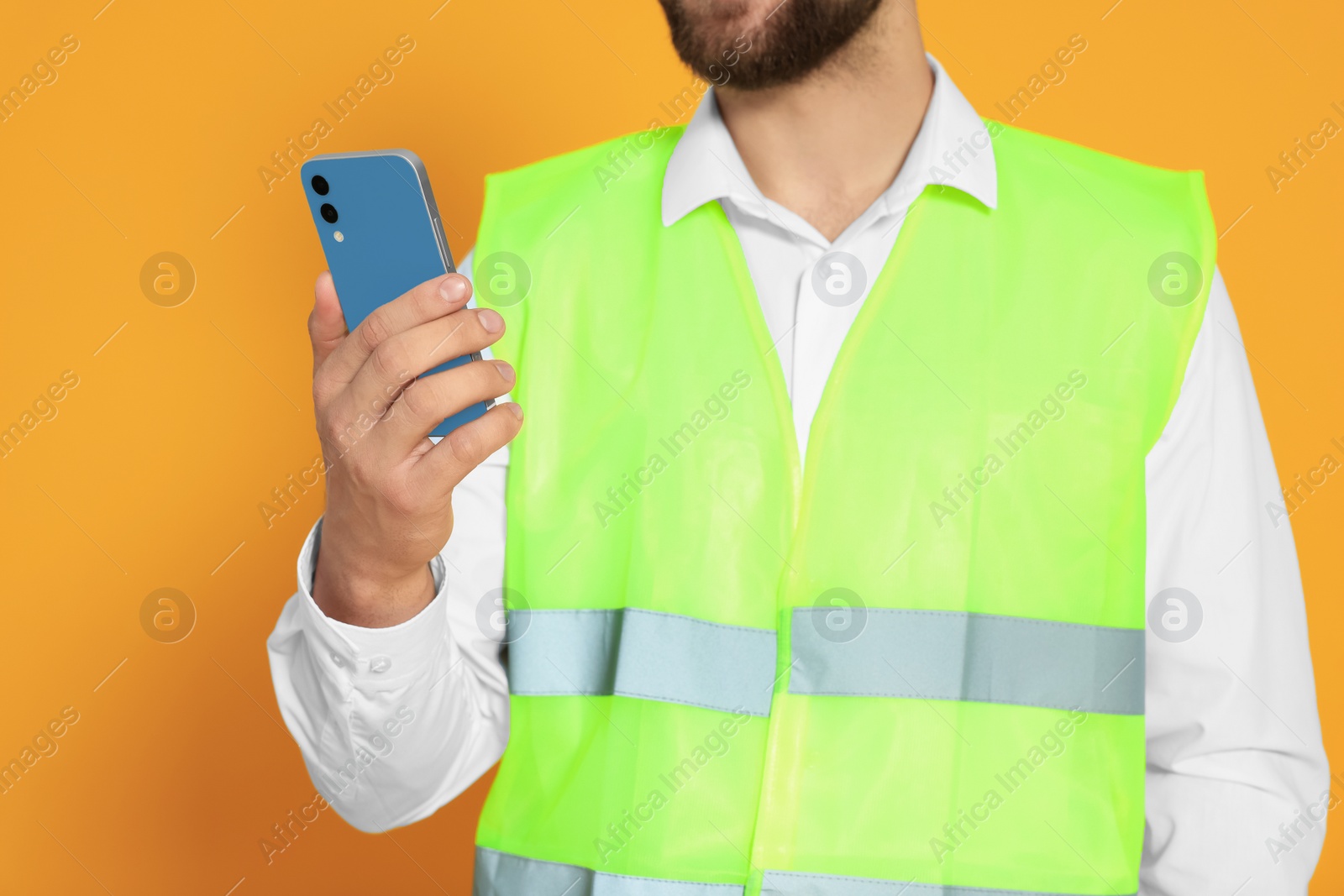 Photo of Man in reflective uniform with smartphone on orange background, closeup