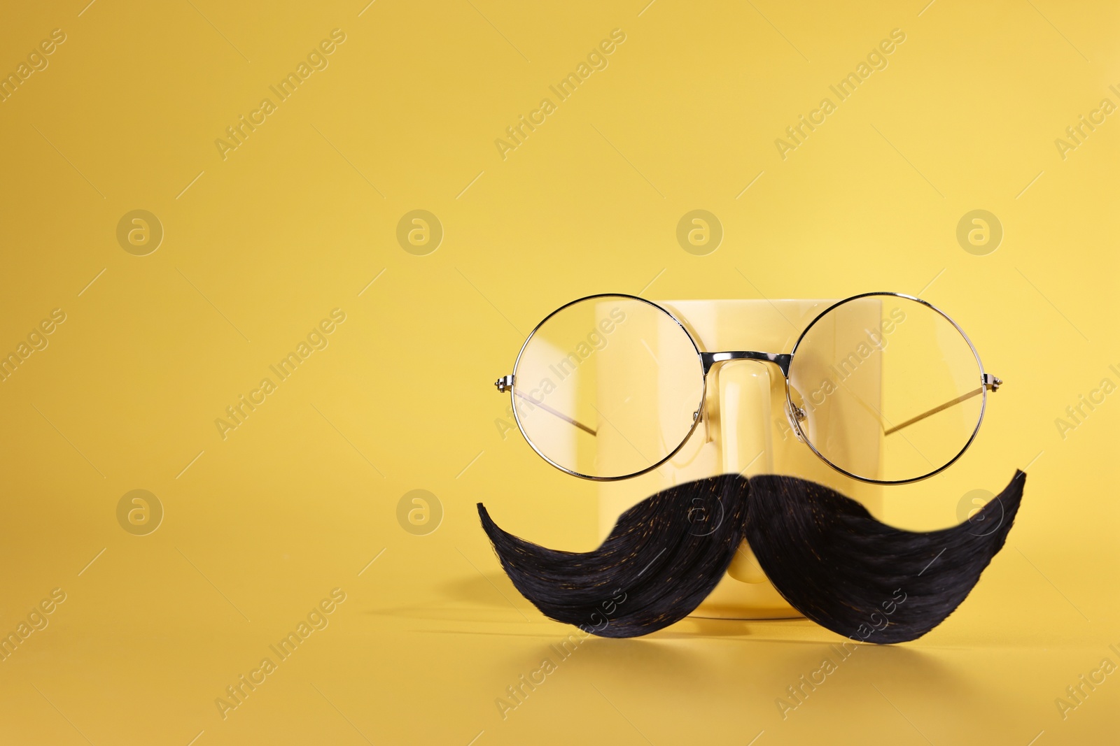 Photo of Man's face made of artificial mustache, glasses and cup on yellow background. Space for text