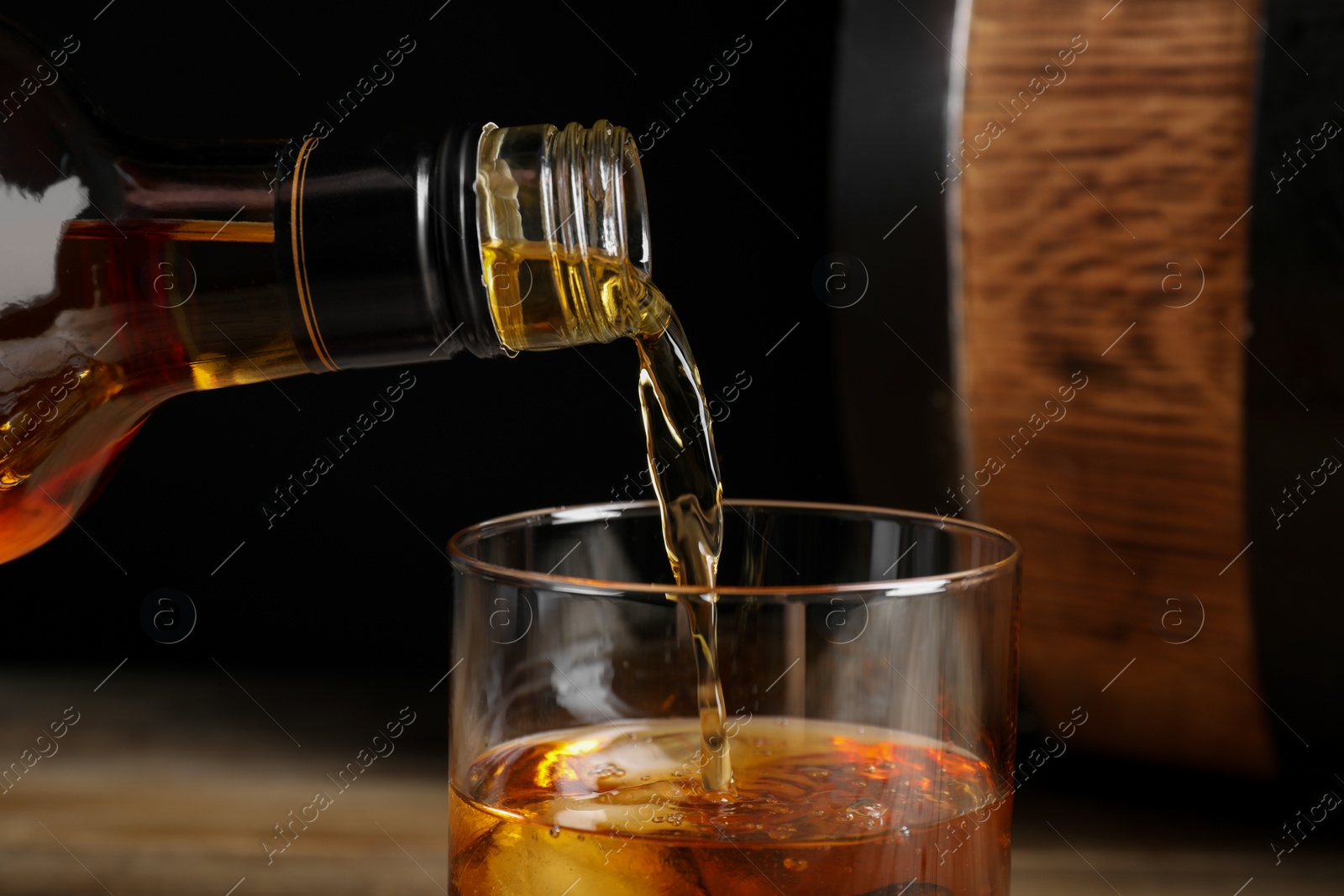 Photo of Pouring whiskey from bottle into glass, closeup