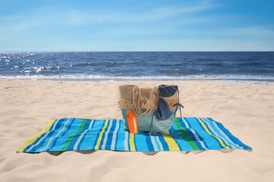 Photo of Striped beach towel and bag with accessories on sandy seashore