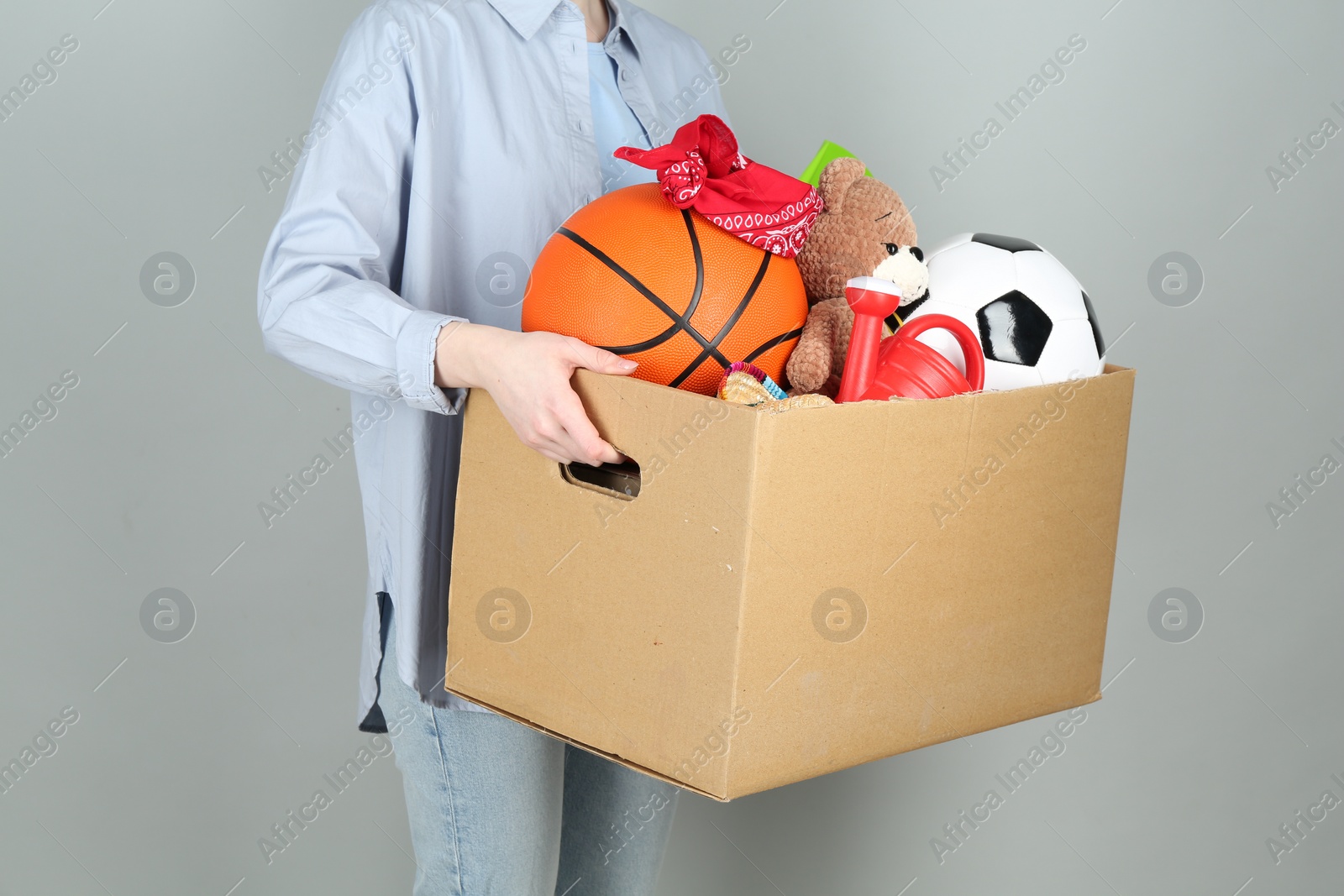 Photo of Woman holding box of unwanted stuff on grey background, closeup