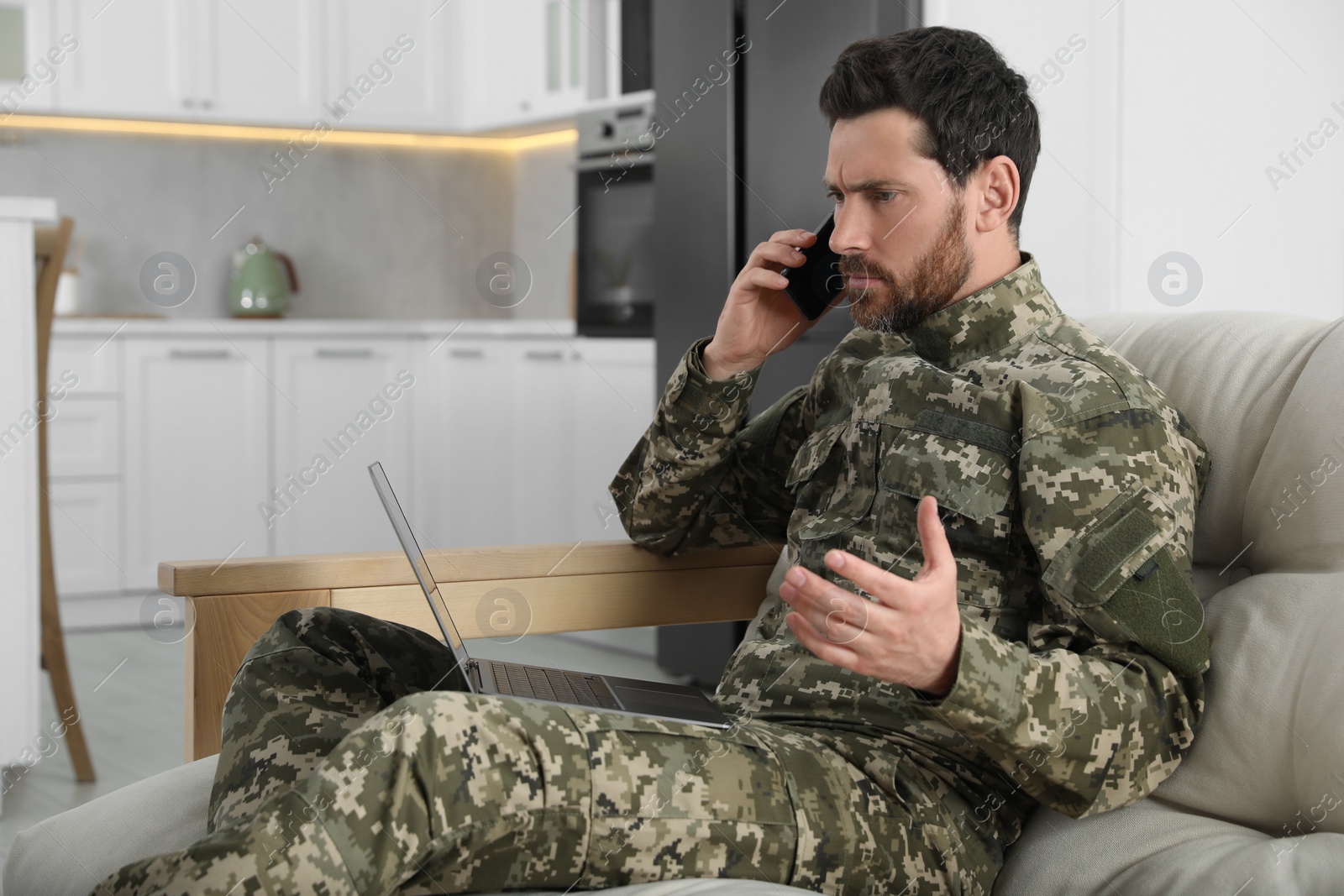 Photo of Soldier with laptop talking on phone at home. Military service