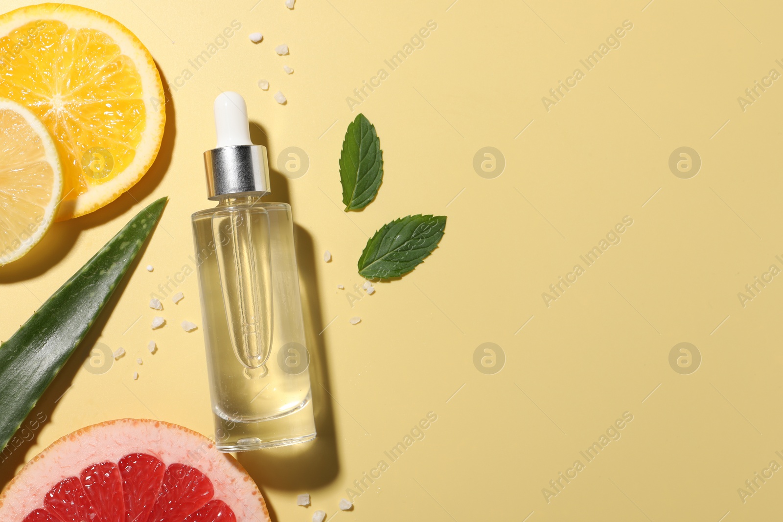Photo of Bottle of cosmetic serum, sliced citrus fruits and aloe vera leaf on yellow background, flat lay. Space for text
