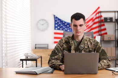 Photo of Military service. Young soldier working with laptop at wooden table in office