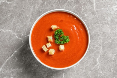 Bowl with fresh homemade tomato soup on grey background, top view