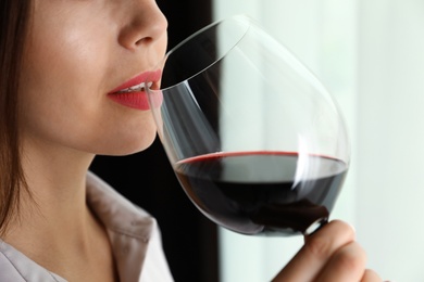 Young woman with glass of luxury red wine indoors, closeup view