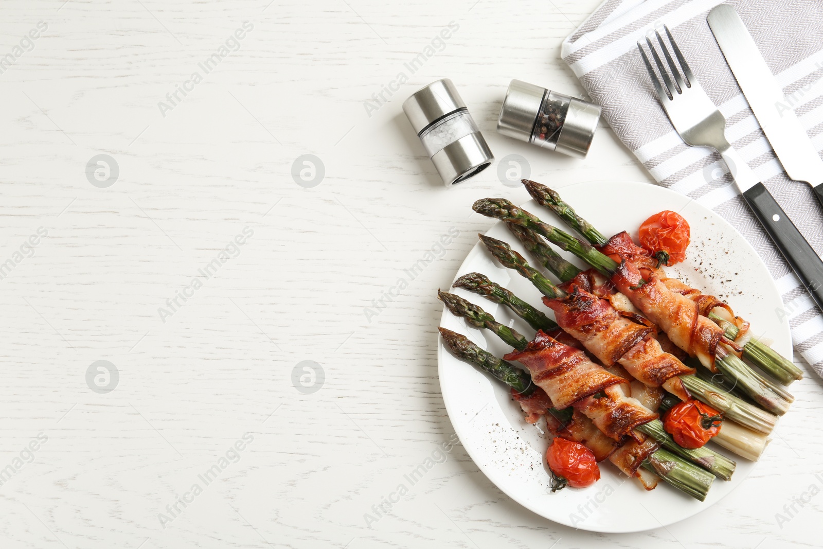 Photo of Oven baked asparagus wrapped with bacon on white wooden table, flat lay. Space for text