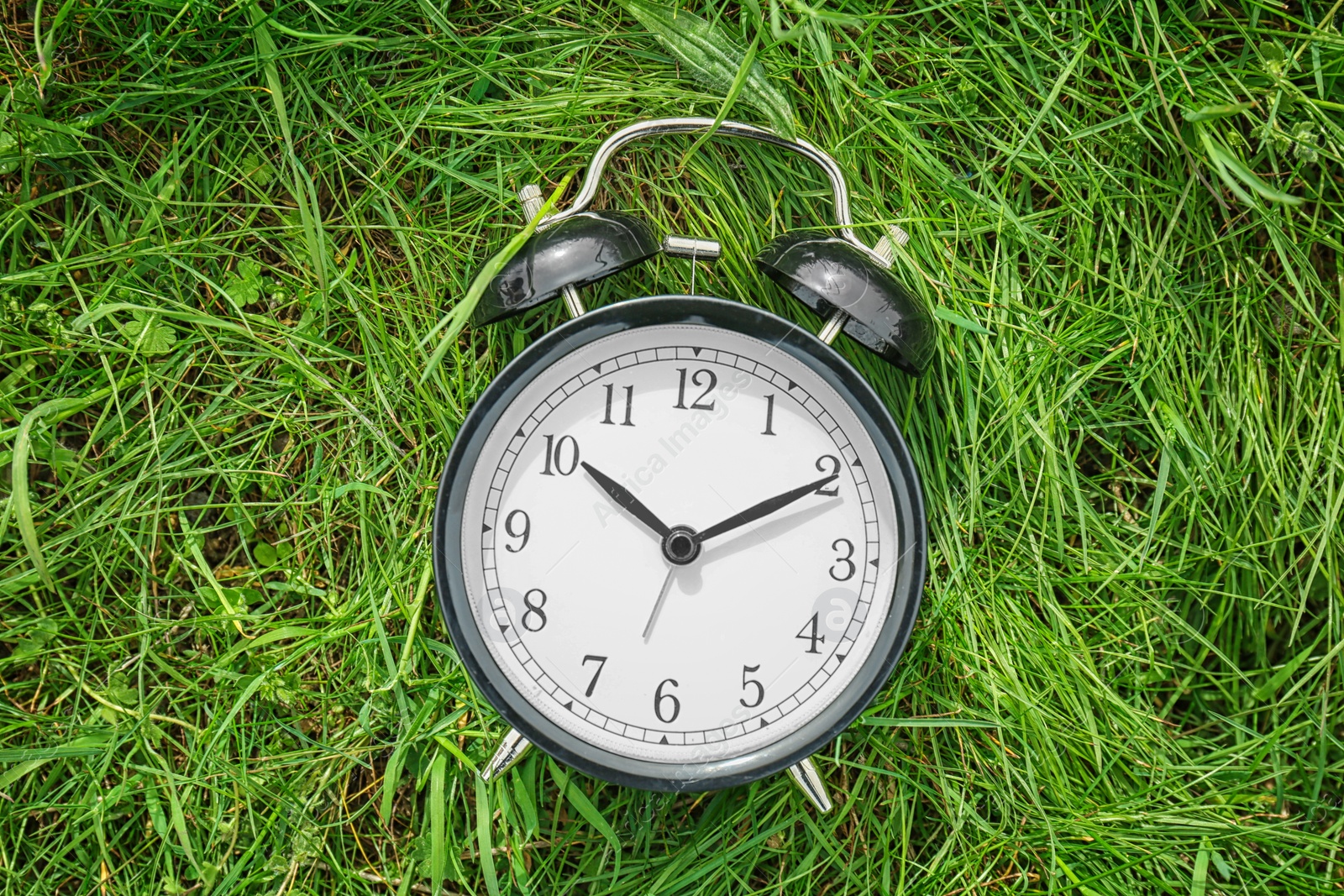 Photo of Alarm clock on green grass, outdoors. Time change concept