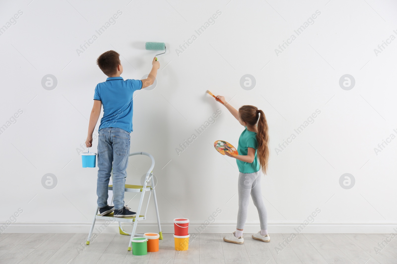 Photo of Little children painting on blank white wall indoors