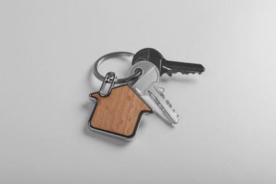 Photo of Keys with trinket in shape of house on white background. Real estate agent services