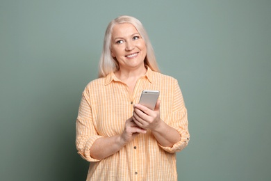 Mature woman using mobile phone on color background