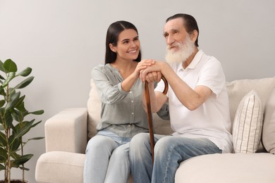 Photo of Senior man with walking cane and young woman on sofa indoors