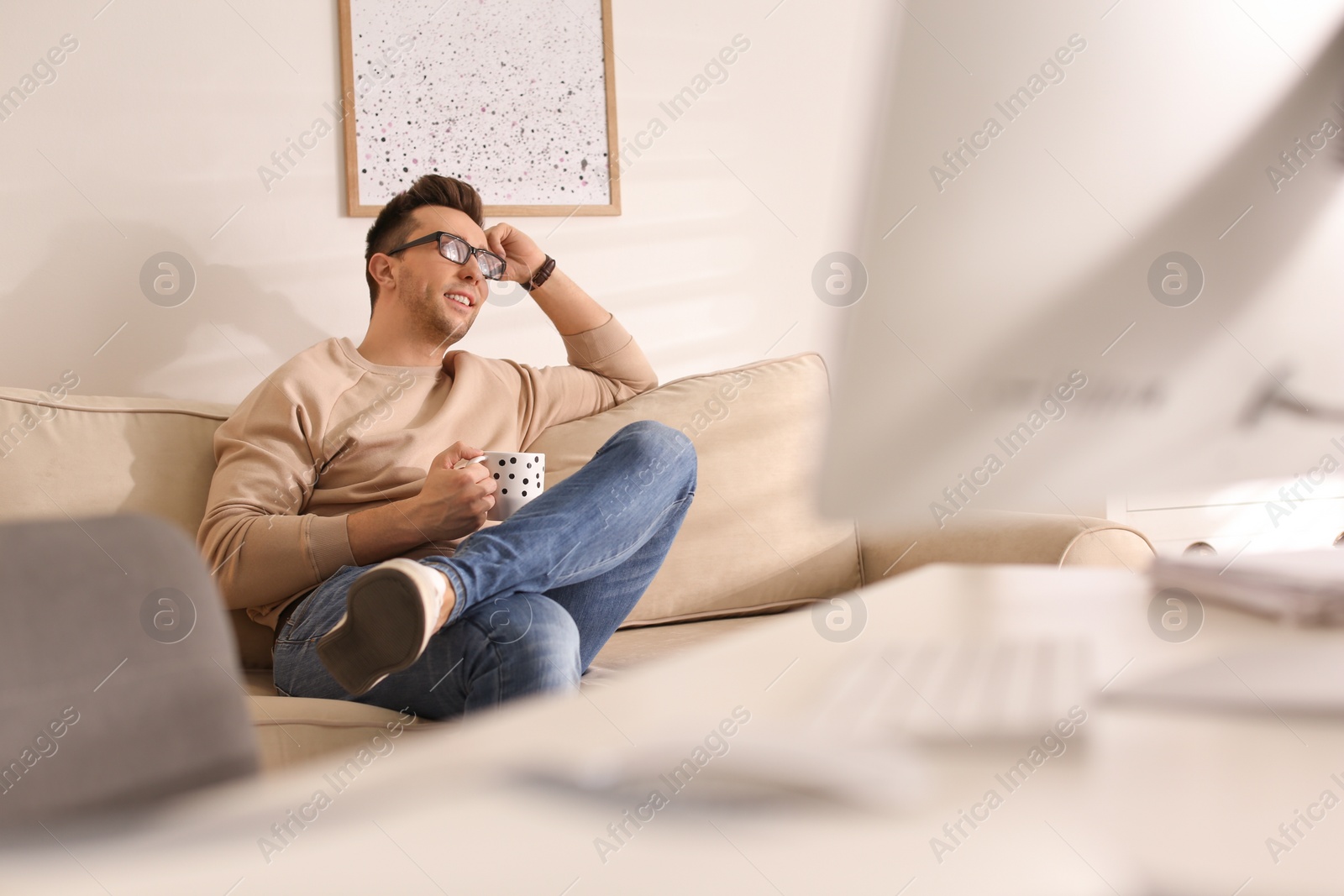 Photo of Young man with cup of drink relaxing on couch in office during break