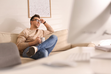 Young man with cup of drink relaxing on couch in office during break