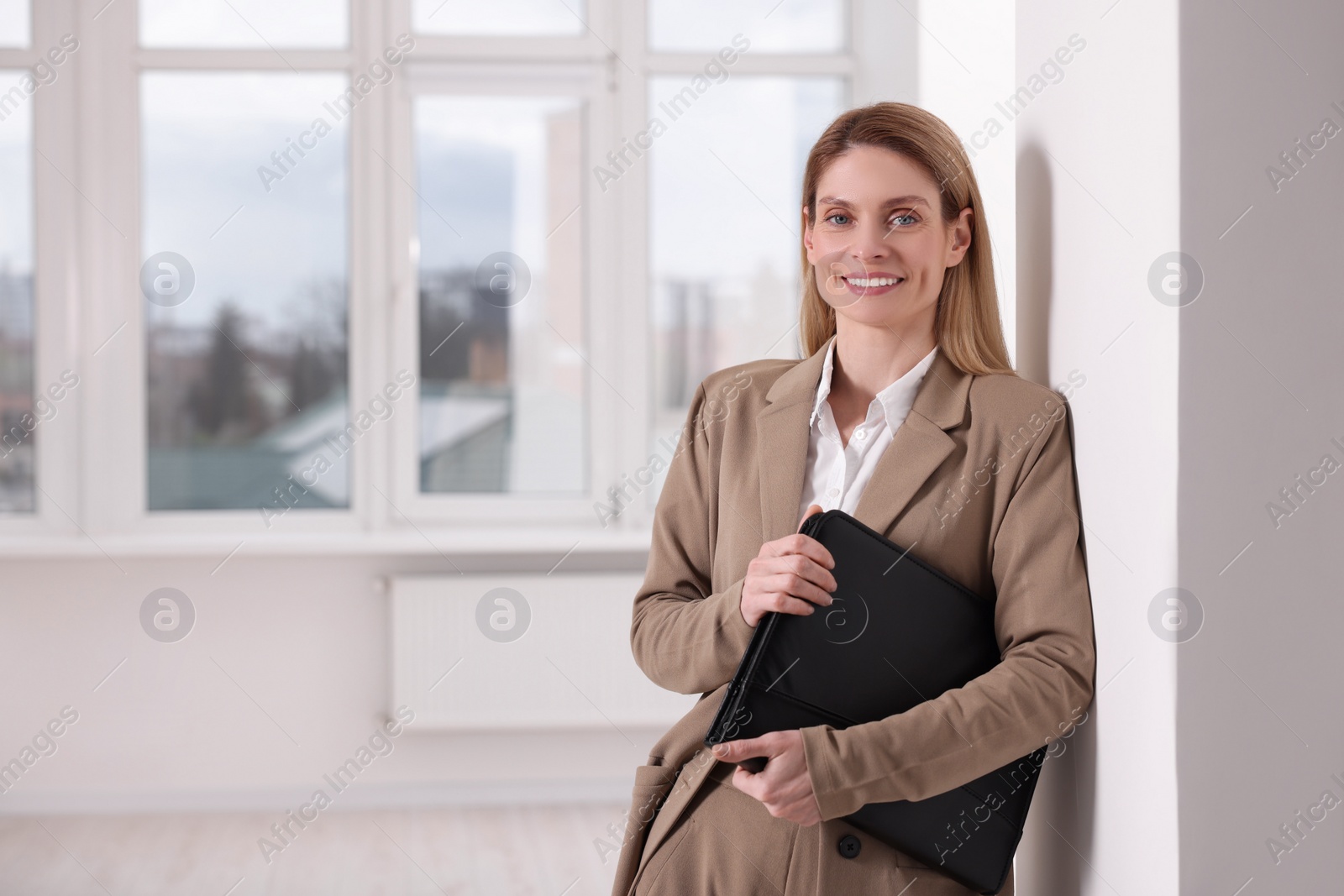 Photo of Happy real estate agent with leather portfolio indoors. Space for text