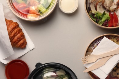 Photo of Tasty food in containers with wooden knife and fork on light grey table, flat lay. Space for text