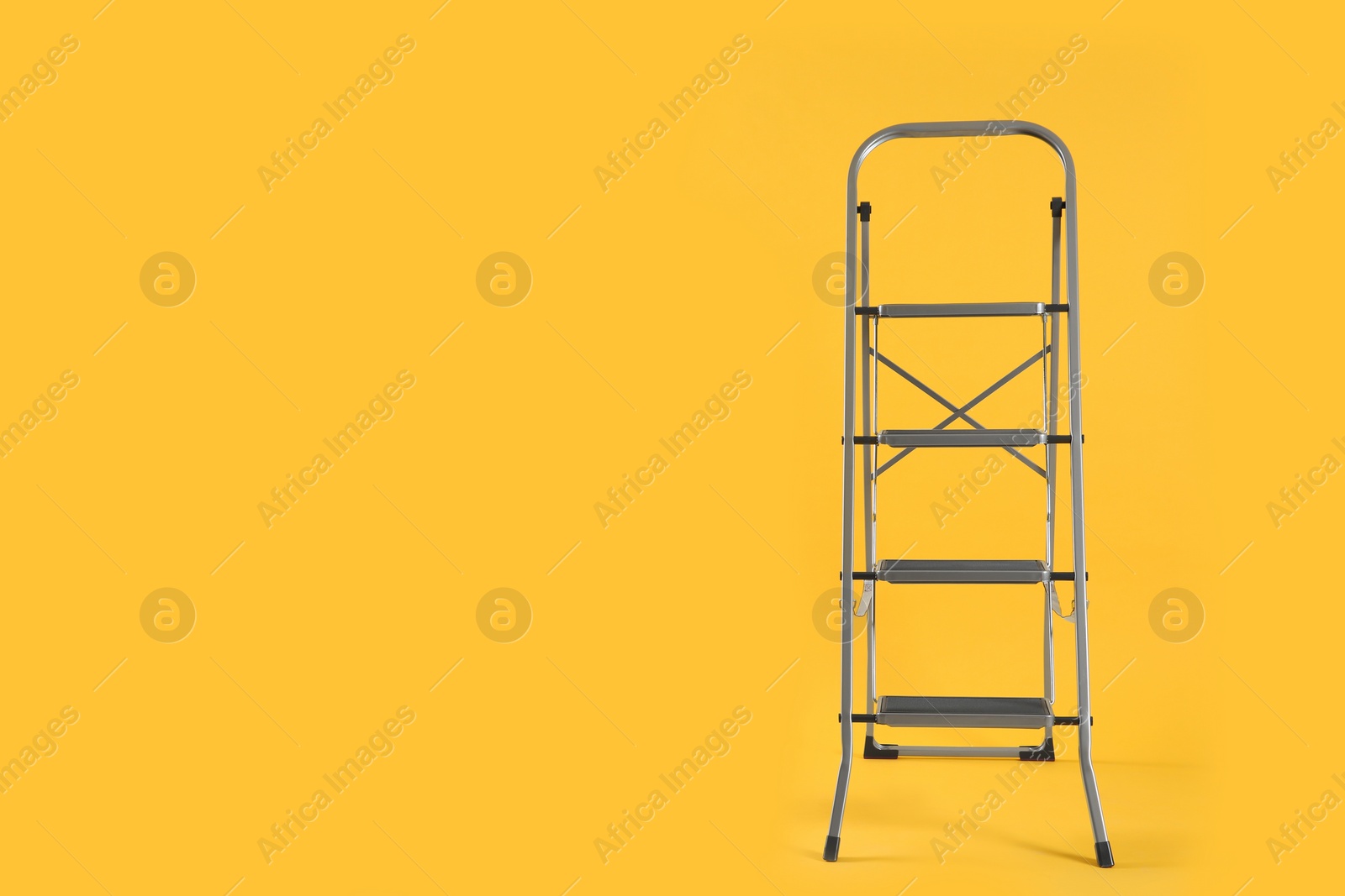 Photo of Modern metal stepladder on yellow background. Space for text