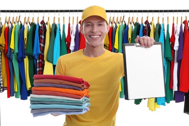 Image of Dry-cleaning delivery. Happy courier holding folded clothes and clipboard near wardrobe rack on white background