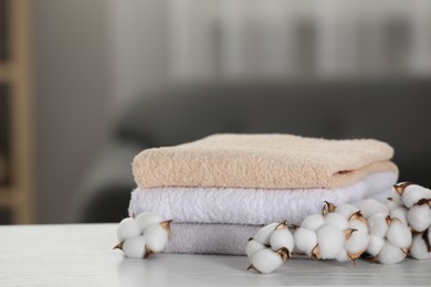 Photo of Terry towels and cotton branch with fluffy flowers on white wooden table in room, closeup