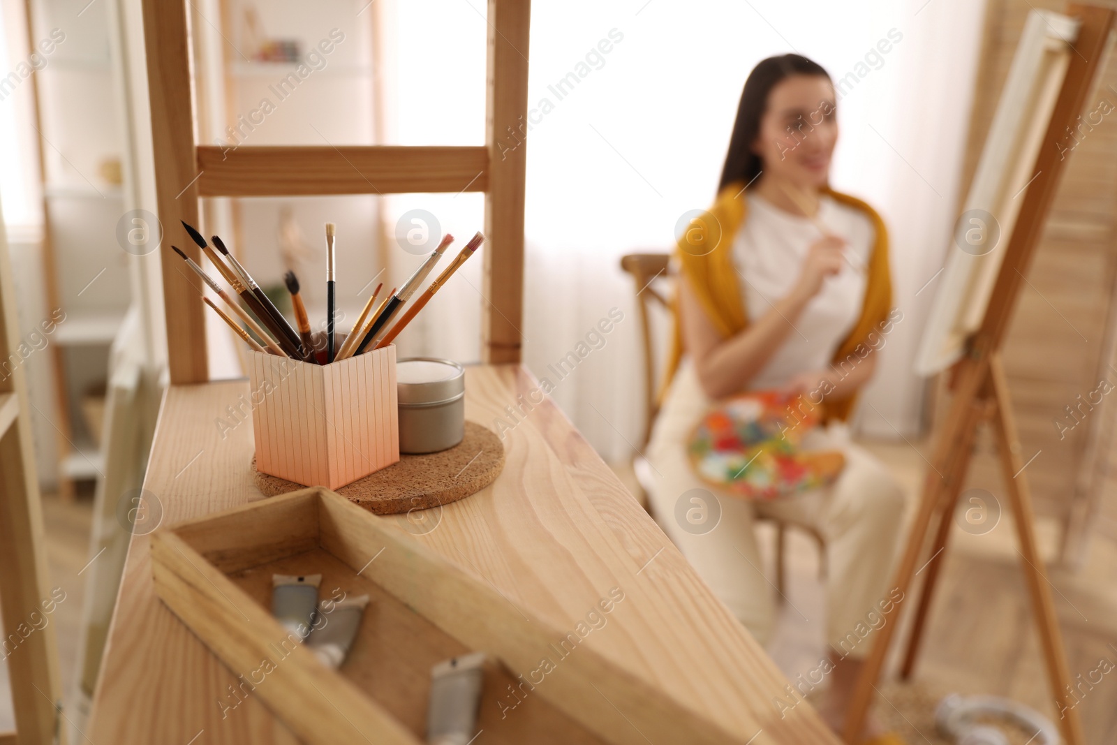 Photo of Beautiful young woman drawing at home, focus on brushes