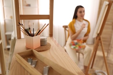 Photo of Beautiful young woman drawing at home, focus on brushes